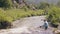 Happy woman sitting on shore of stony river and resting while trekking.