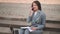 Happy Woman sitting on stairs while talking on phone, working with papers documents on laptop in the street.