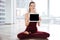 Happy woman sitting in yoga pose showing blank screen tablet