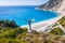 Happy woman standing on top of a rock, raising hands with an exciting feeling of freedom, looking at Myrtos Beach