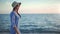 Happy woman in straw hat and sunglasses walking on seashore at sunset. Medium shot on RED camera