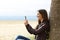 Happy woman texting in the phone on the beach in winter