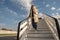 Happy woman traveler in sunglasses going down on aircraft stairs after landing at airport