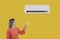 Happy woman uses remote control to turn on modern air conditioner on yellow background