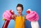 Happy woman using bottles of cleaning detergent as guns on blue