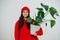 Happy woman in vibrant red cap and hoodie holding pot with monstera