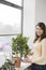 Happy Woman Watering Plants At Window Sill