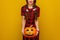 Happy woman on yellow background holding jack-o-lantern pumpkin
