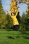 Happy woman in yellow coat jumping in autumn park