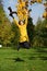 Happy woman in yellow coat jumping in autumn park