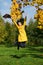 Happy woman in yellow coat jumping in autumn park