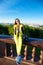 Happy woman in a yellow jumpsuit sits on the railing against the backdrop of the Sparrow Hills in Moscow