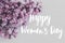 Happy women`s day floral greeting card. Handwritten greetings on tender lilac flowers close up on white wood in soft light.