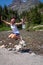 Happy young adult woman wearing american flag patriotic clothing jumps by Running Eagle Falls waterfall in Glacier National Park