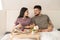 Happy young affectionate husband and wife in t-shirts sitting in bed and talking during breakfast