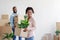 Happy young african american female and male carry cardboard boxes with plants to room with white walls