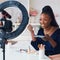 Happy young african american woman streaming a beauty vlog from home, online content creator applying a makeup on