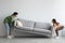 Happy young Asian couple moving sofa in living room, replacing furniture at home, copy space