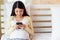 Happy young asian pregnant woman using and browsing online information of prenatal care on smartphone. Pregnancy mother sitting on