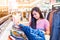 Happy young asian woman checking a price tag on shirt in mall or clothing store