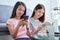 Happy young Asian woman with friends sitting on sofa and reading book, using smartphone in her living room, vacation time.