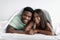 Happy young attractive african american guy and lady lie on bed under covers in bedroom