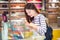 Happy young attractive asian woman shopping and looking at merchandises in glass display cabinet deciding which one to buy