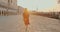 Happy young back lit attractive Caucasian tourist woman walks to camera at empty summer sunrise square in Venice Italy.