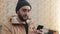 Happy young beard man using smartphone in the street near shopping mall. He is wearing an autumn jacket and knitted hat