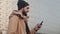 Happy young beard man using smartphone walking in the street near shopping mall. He is wearing an autumn jacket and