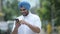 Happy young bearded Indian Sikh man using phone outdoors
