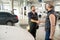 Happy young bearded technician of car service shaking hand of male client