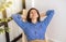 Happy young beautiful smiling woman sitting on a wooden chair, raising her arms, stretching her back muscles, enjoying a carefree