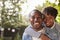 Happy young black couple piggyback in garden, look to camera