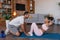 Happy young black guy helps his wife in sportswear to do exercises for abs on mat in living room interior, profile