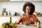 Happy young black lady preparing healthy vegetable salad in kitchen, adding salt