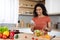 Happy young black lady in red t-shirt prepares food with organic vegetables, types on phone, reads message