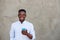Happy young black man with mobile phone standing by wall