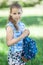 Happy young blonde hair girl standing in park with small backpack in hands, looking at camera