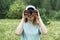 Happy Young blonde woman bird watcher in cap and blue t-shirt looking through binoculars at cloudy sky in summer forest