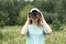 Happy Young blonde woman bird watcher in cap and blue t-shirt looking through binoculars at cloudy sky in summer forest