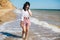 Happy young boho woman walking and having fun in sea waves in sunny warm day on tropical island. Summer vacation. Space for text.