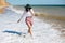 Happy young boho woman walking in sea waves in sunny warm day at tropical island and blue sky. Space for text. Stylish hipster