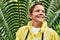 Happy young boy in raincoat standing in front of large fern during field trip