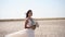 Happy young bride with bouquet of flowers going at desert landscape. Elegance lady in gorgeous wedding dress walks in