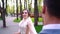 Happy young bride walking around groom standing still in sunny park