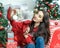 Happy young brunette female decorating christmas tree. Girl sitting and holding a christmas ball in her hands