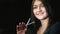 Happy young brunette hairdresser holding scissors while standing in front of camera against black background