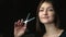 Happy young brunette hairdresser holding scissors while standing in front of camera against black background