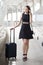 happy young business woman walking and carrying hand luggage using mobile phone . traveling girl with suitcase and  smartphone in